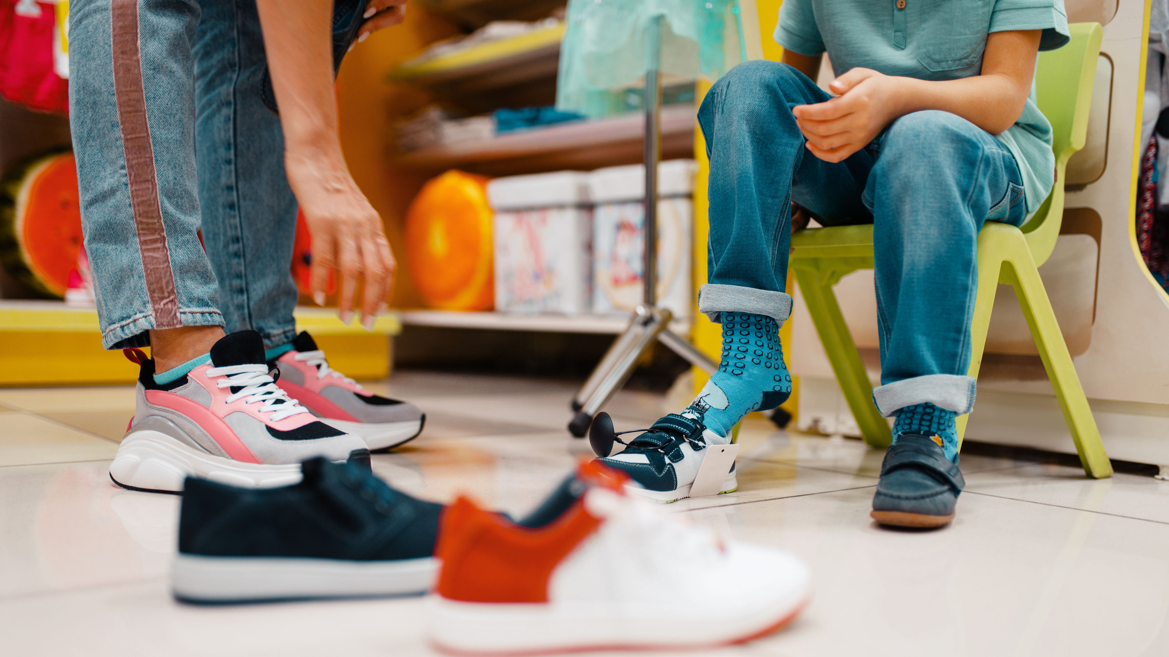 Child trying on sneakers with blue socks, assisted by an adult in a colorful shoe store.