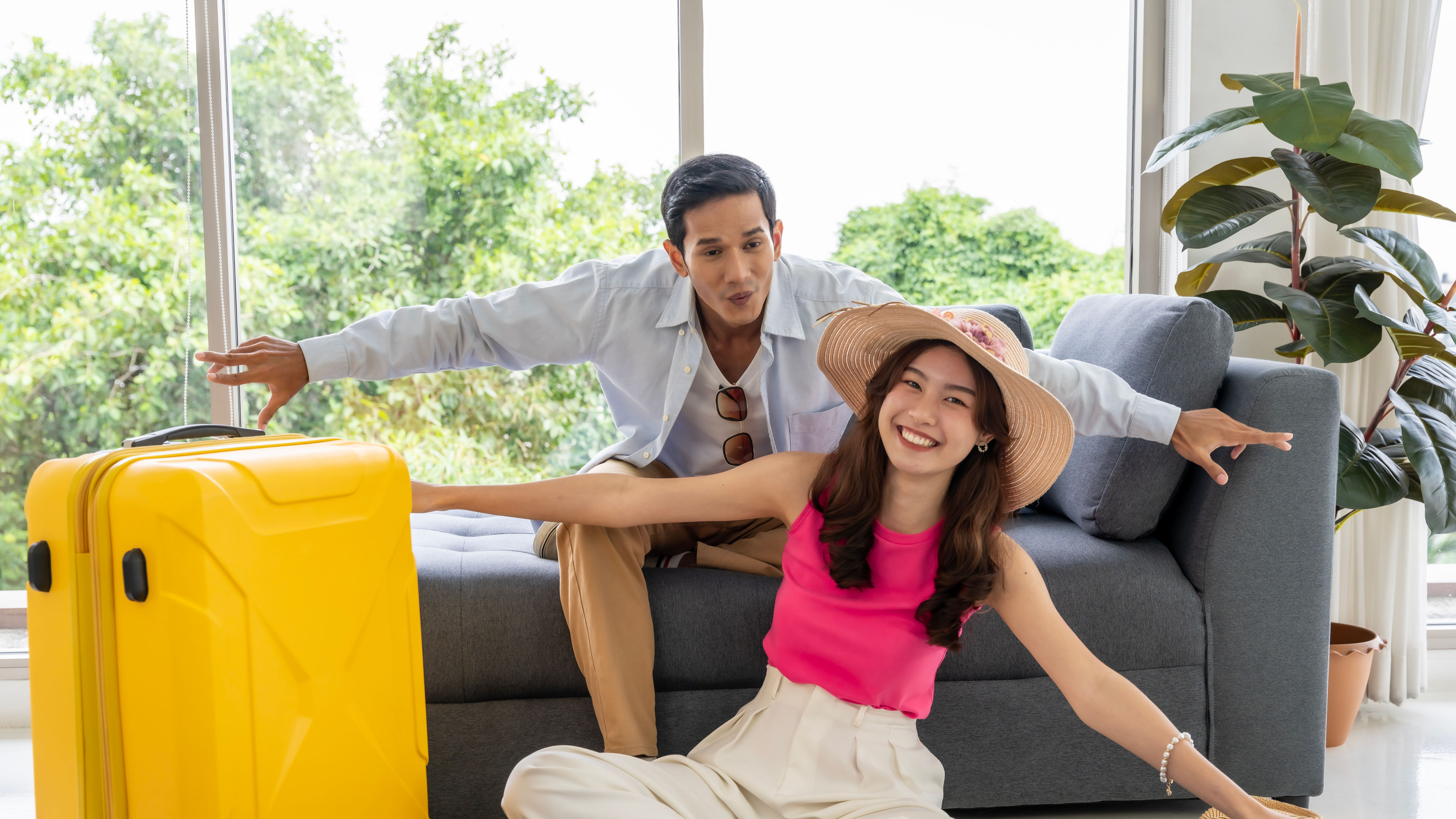 Happy Asian couple preparing to travel together with a yellow trolley bag beside.