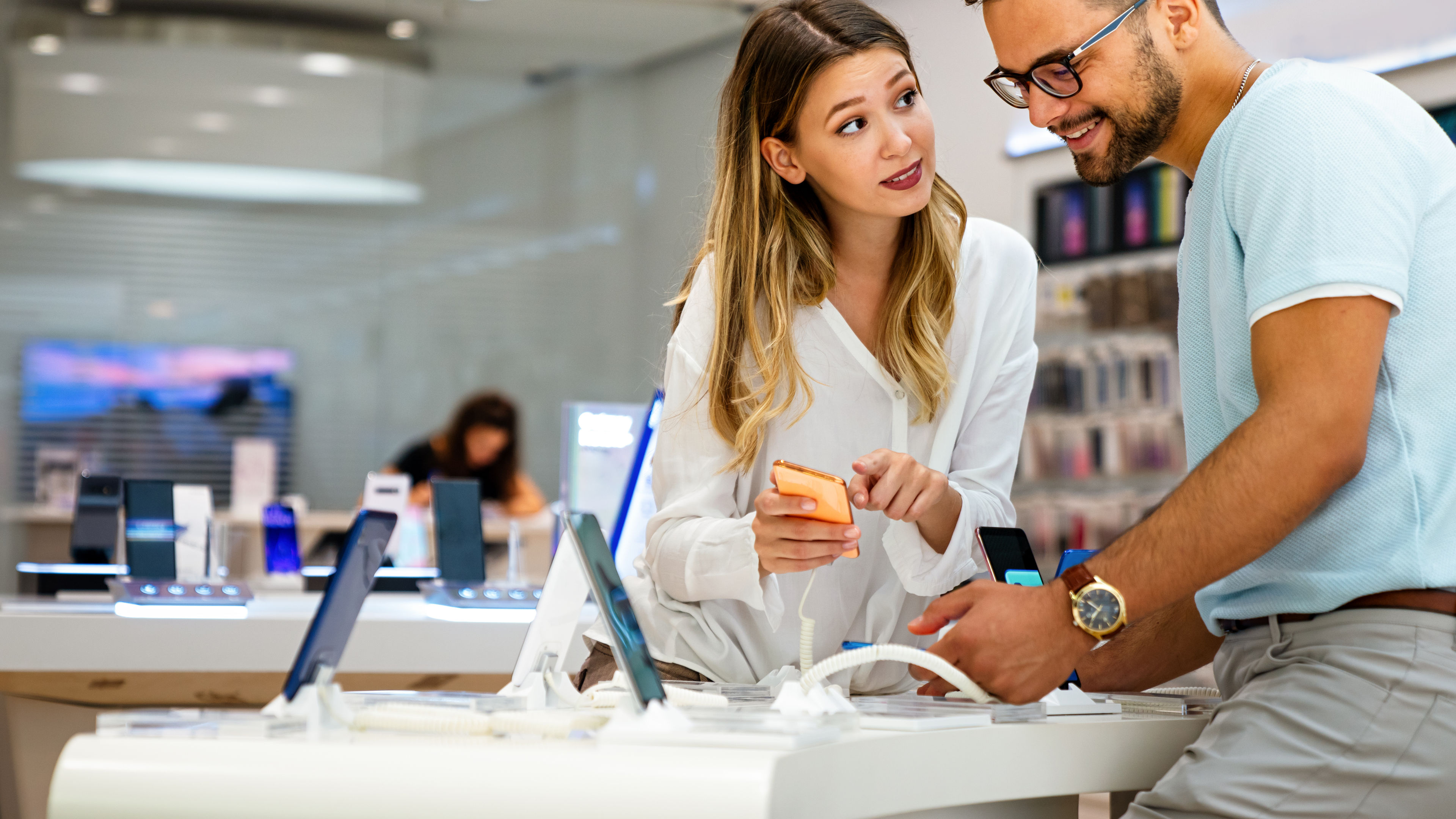 A happy young couple in white and light blue buying new smartphone in mobile shop. 