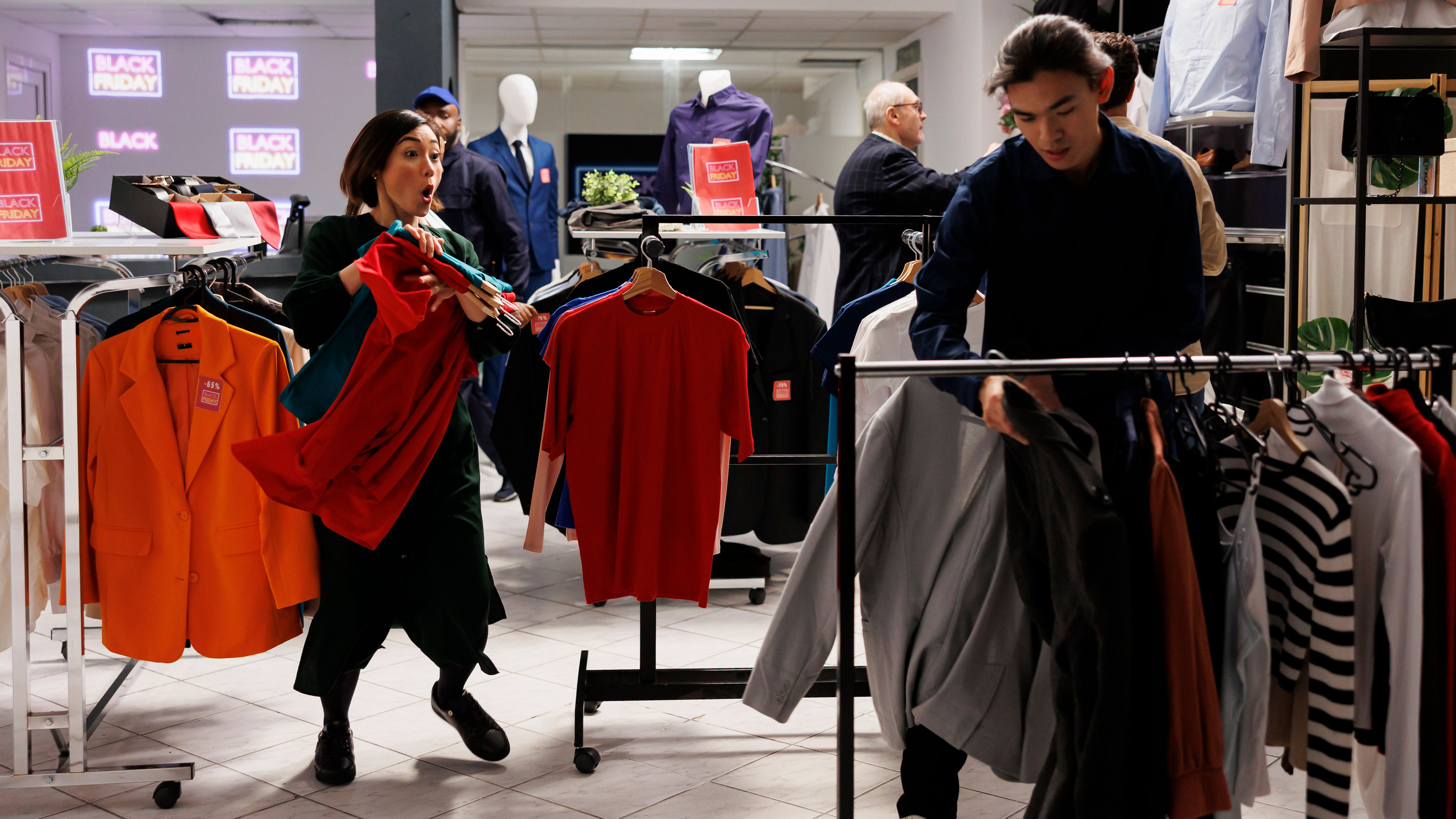 A saleswoman watches curiously as a man browses through a rack of T-shirts.