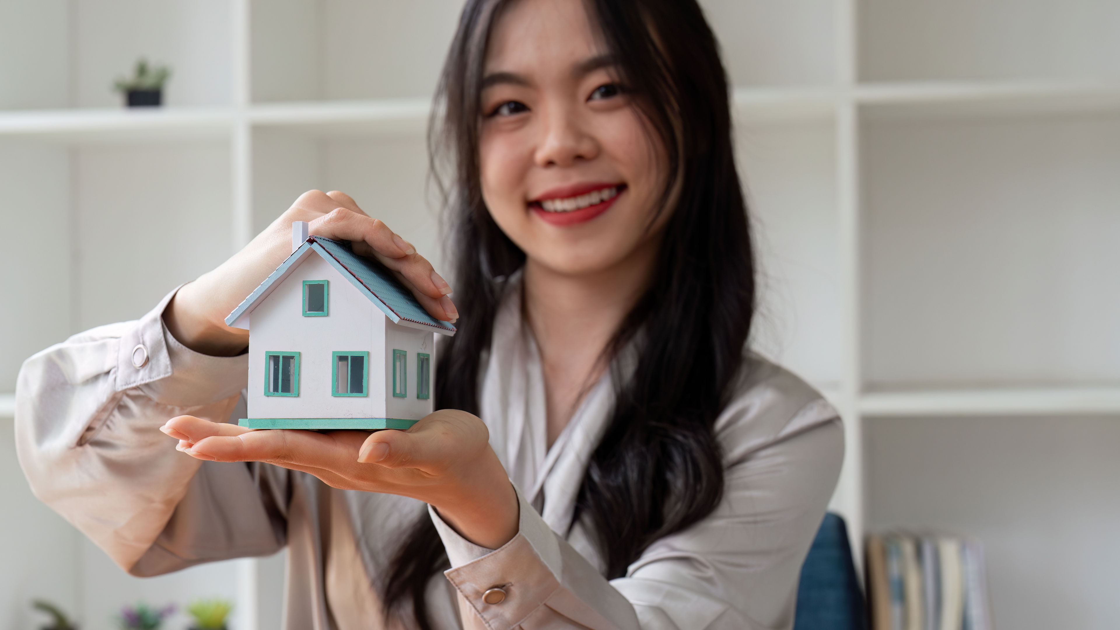 Smiling Asian woman holding miniature house model in hands.