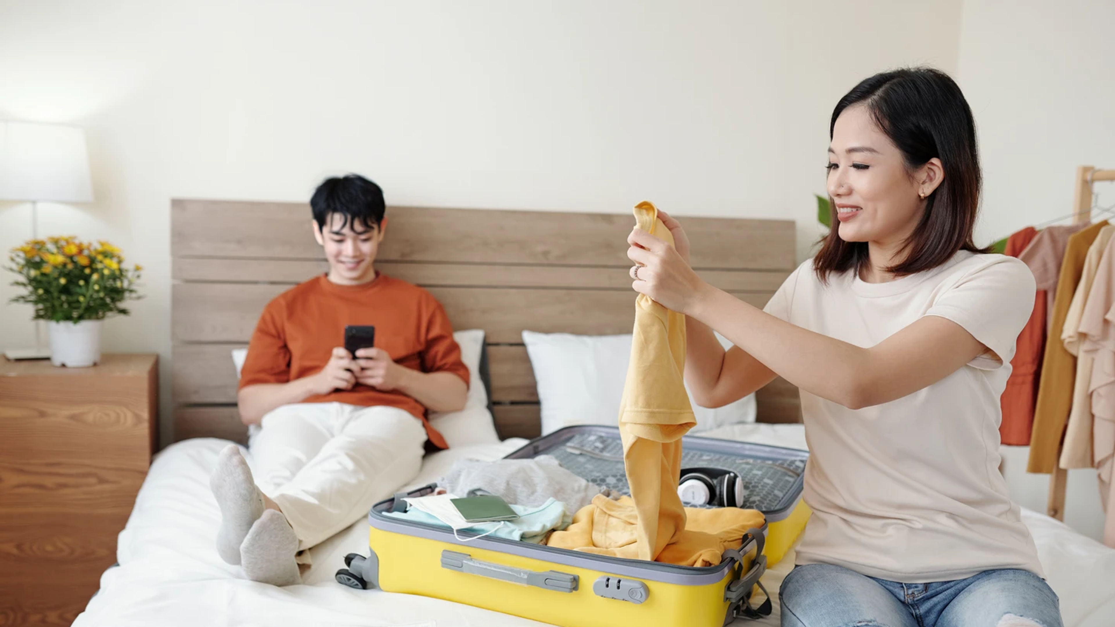 Cheerful pretty young woman folding clothes when packing suitcase for vacation.