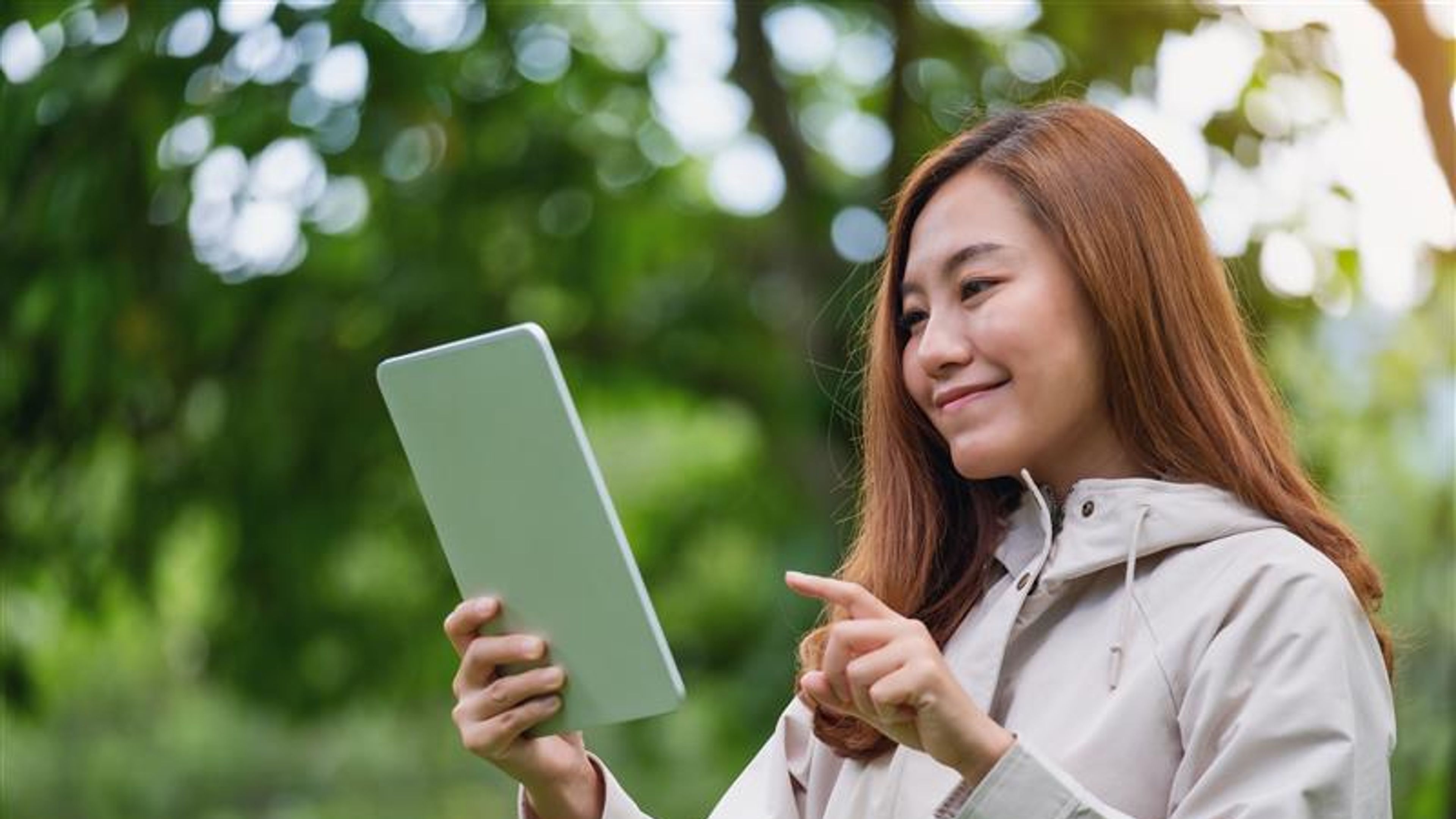 A beautiful young asian woman holding and using digital tablet in the outdoors