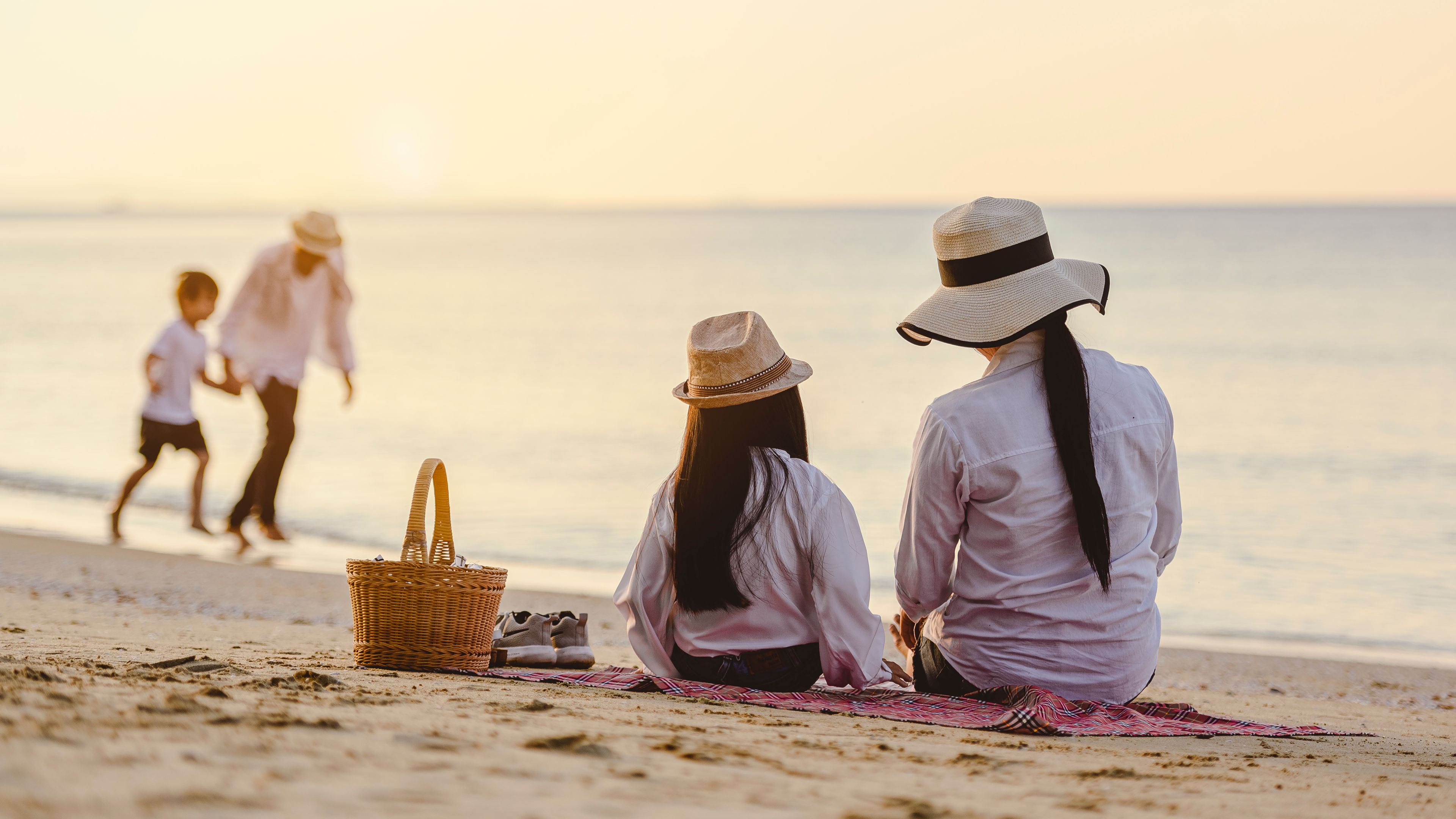 A mother and daughter are sitting on a mat by the beach.