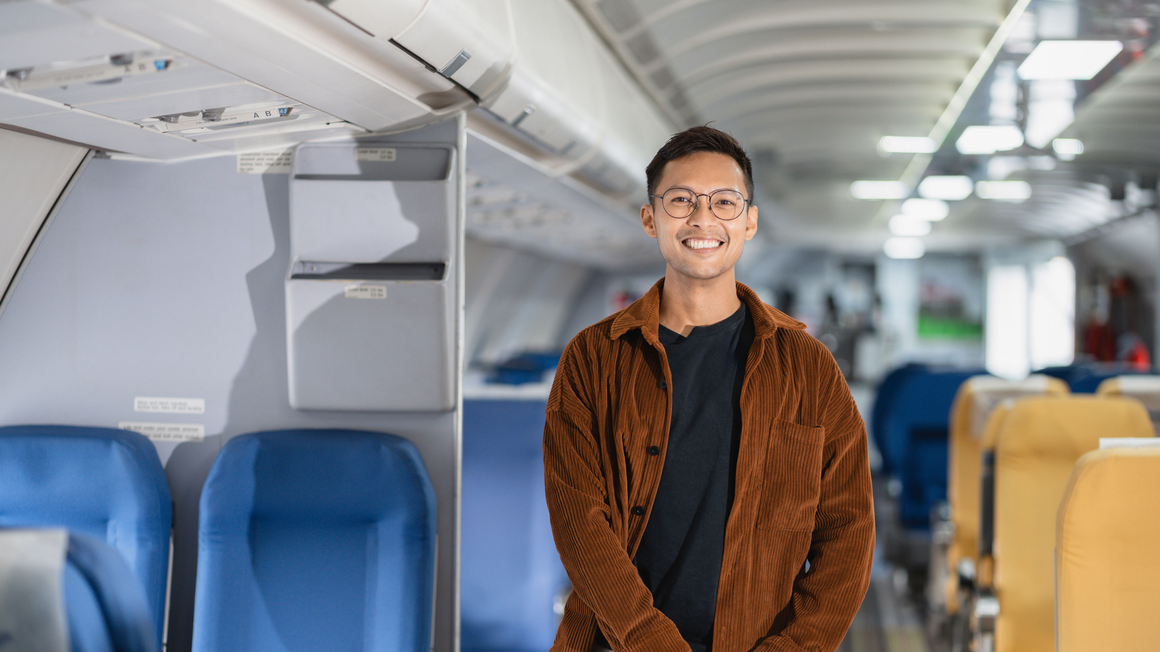 A smiling young man stands inside an airplane cabin