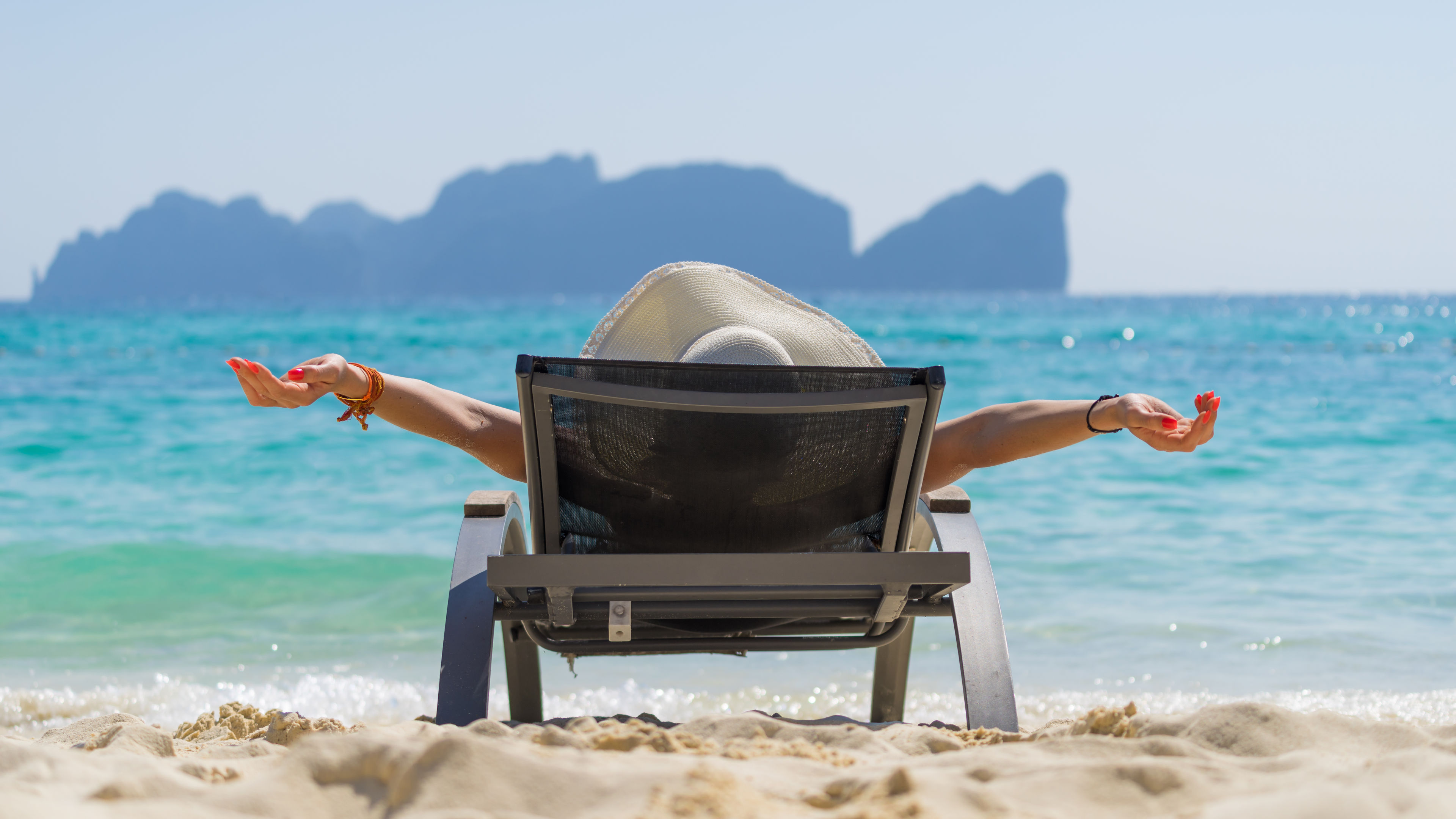 A woman wearing a sun hat relaxes on a lounge chair