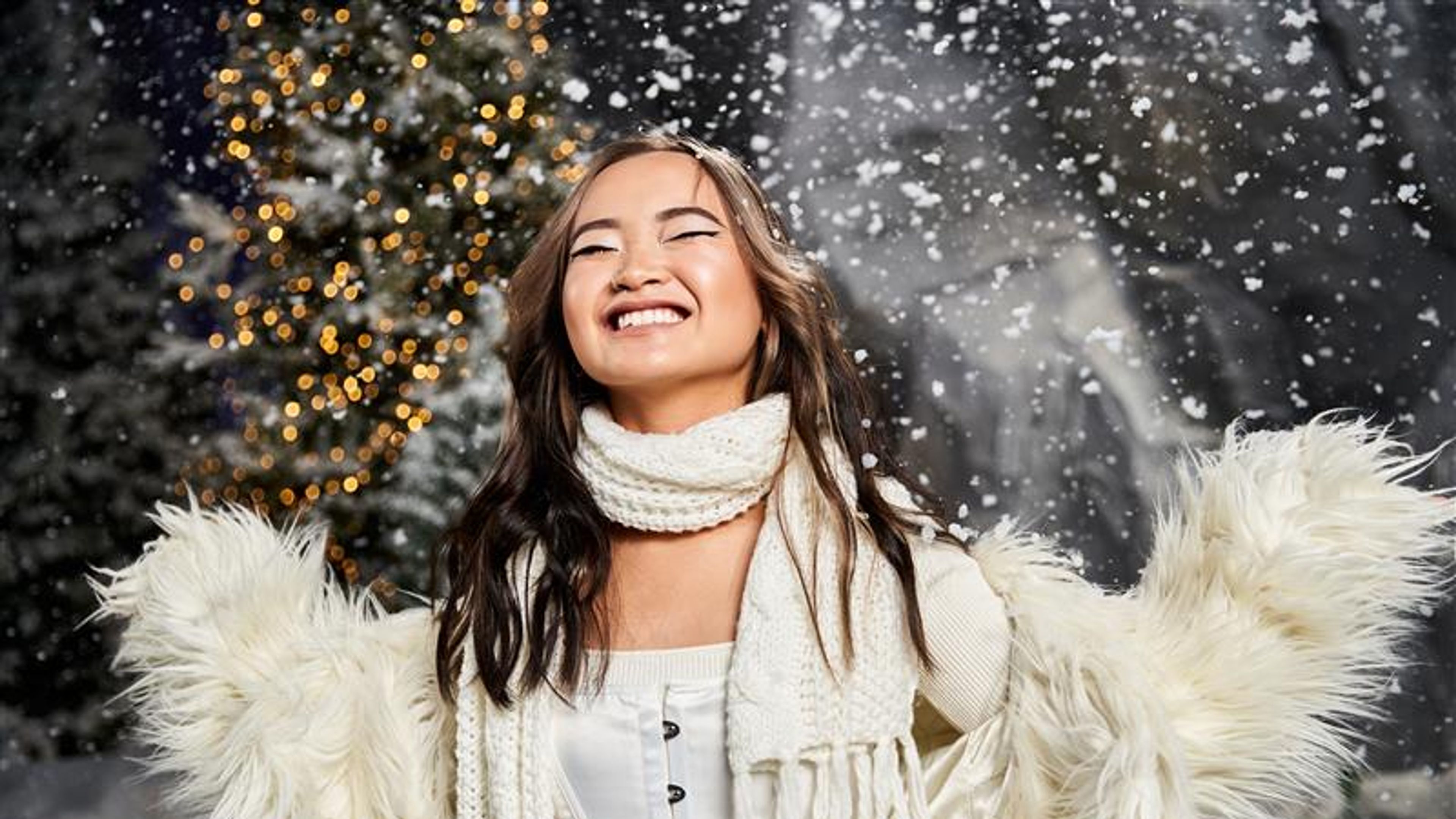 A young woman gleefully enjoys the snowy atmosphere, surrounded by twinkling lights and trees.