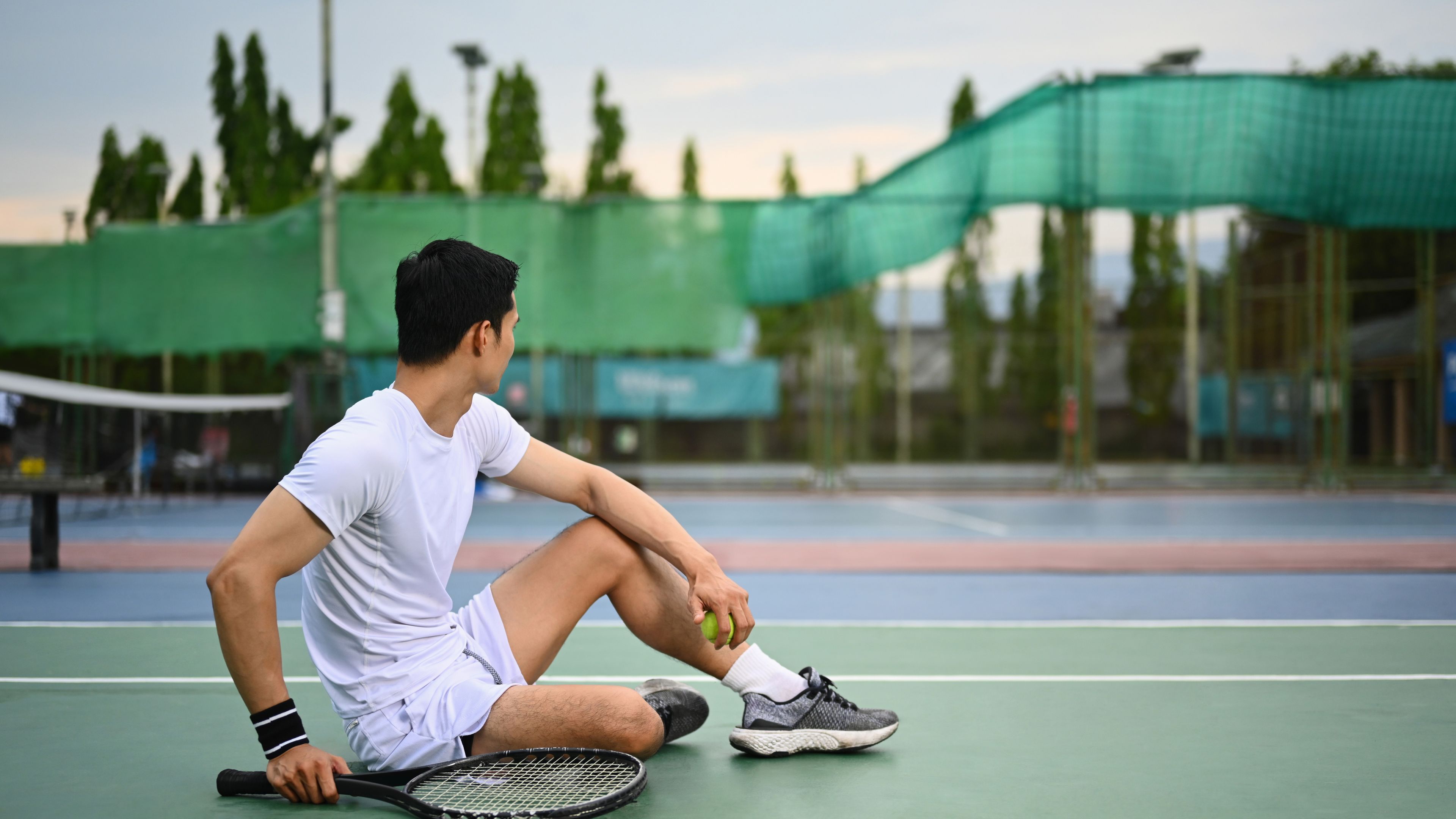 Portrait of sporty man with a tennis racket sitting on a tennis court
