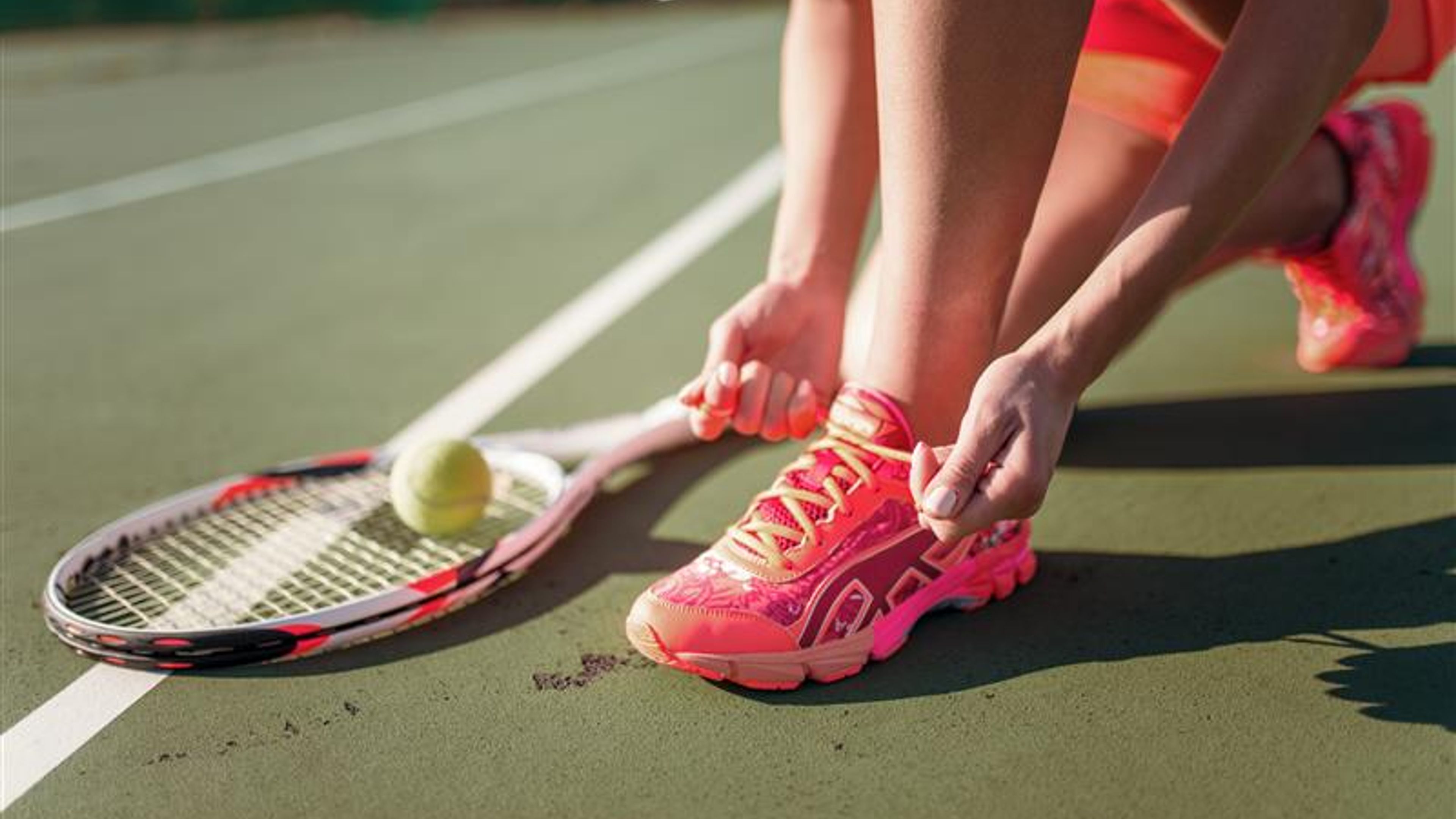 Tennis player tying laces on sneakers, racket and ball on the ground. 