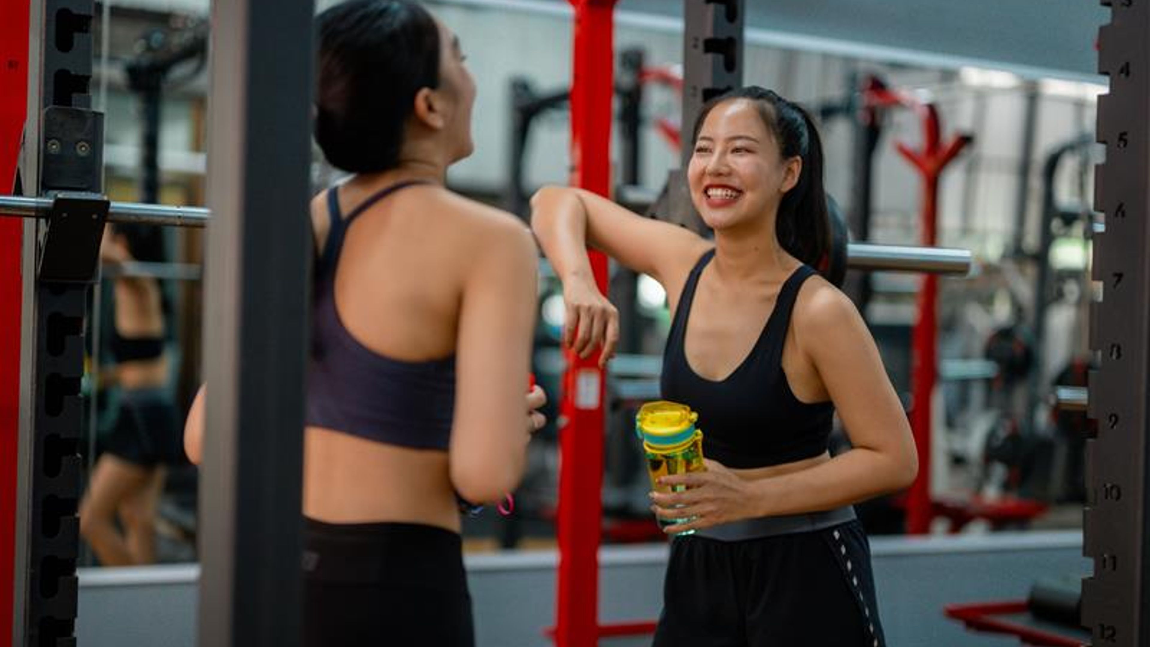 Two young women chatting and smiling at the gym after training