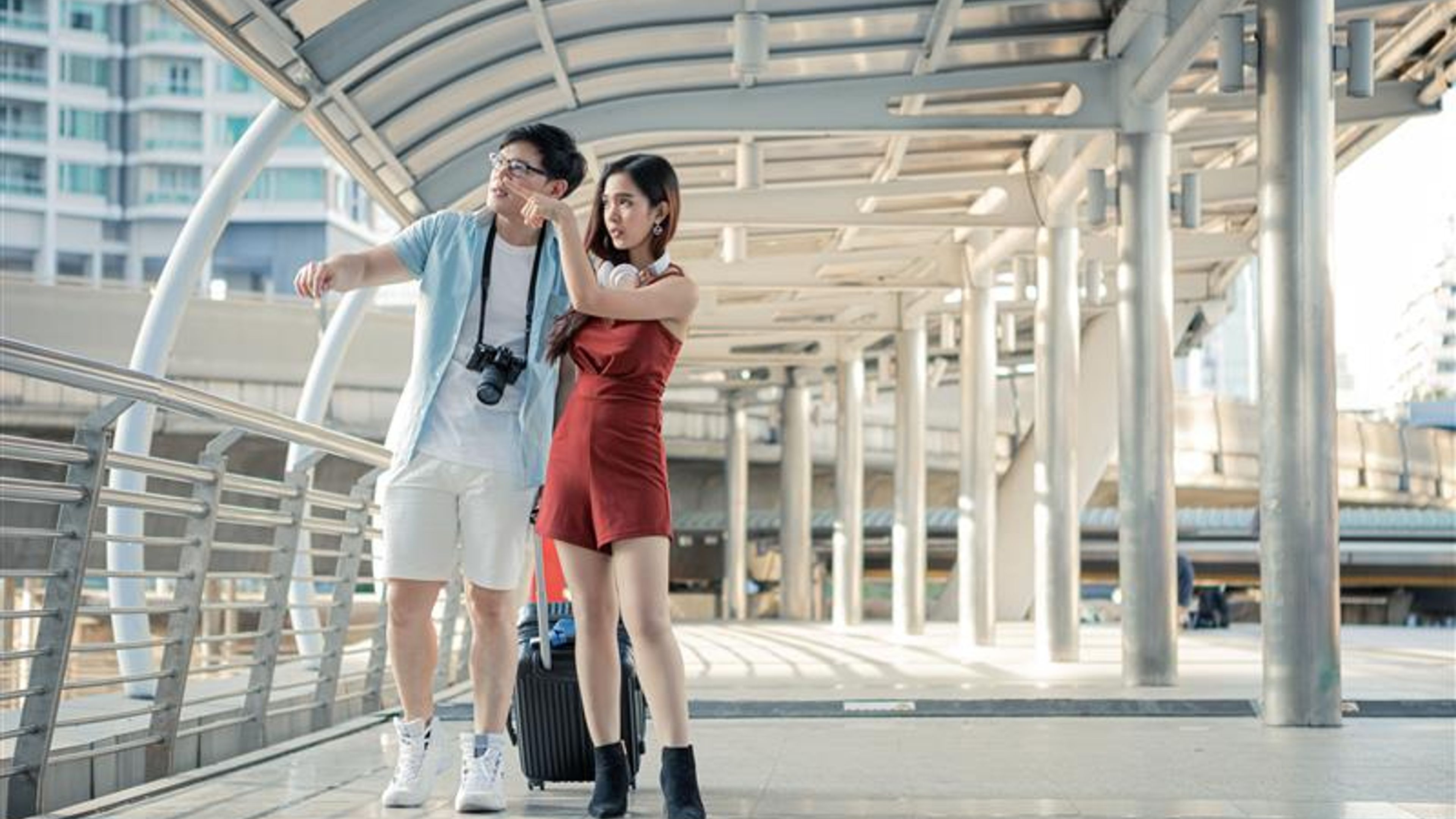 Young couple with dragging a suitcase and talking happily with smiling while to travel in the city.